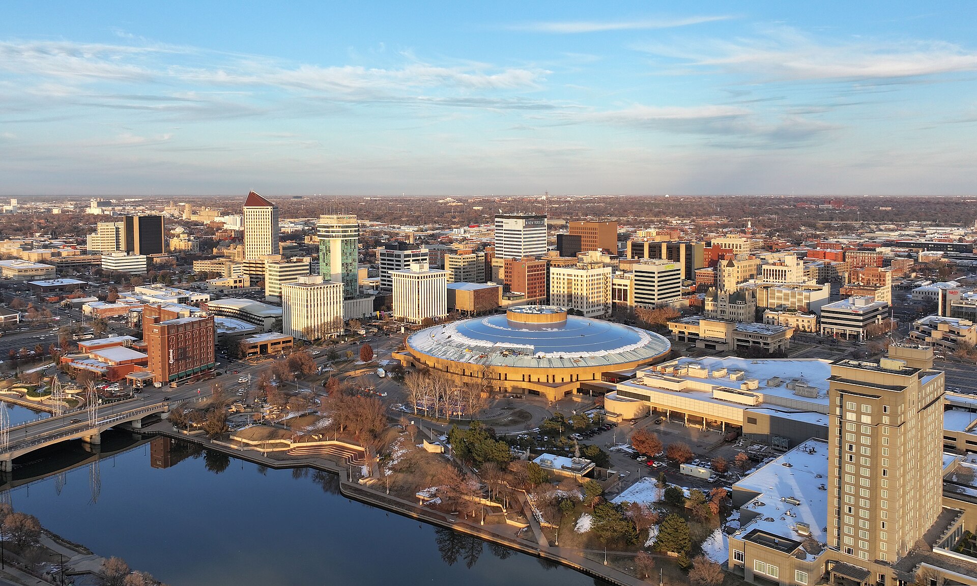 Downtown Wichita and the round Century II hall beside the Arkansas River, seen from above in late-day sun.