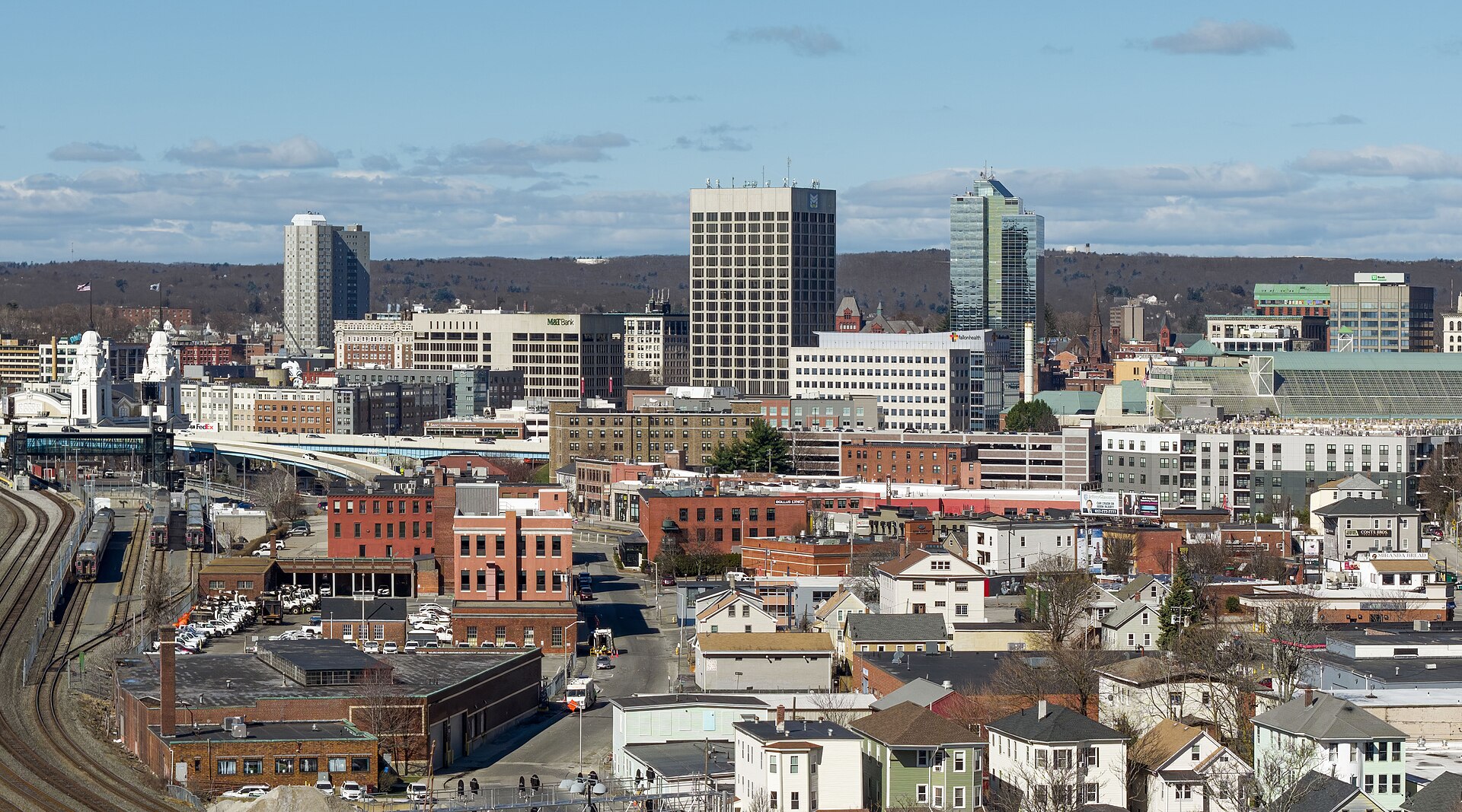 Downtown Worcester office towers rising beyond brick buildings, rail tracks and triple-decker houses on a clear day.