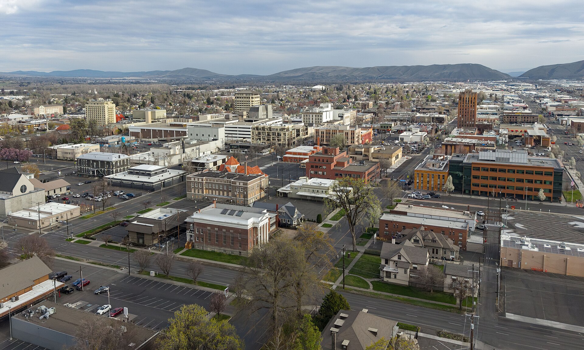 Downtown Yakima's low-rise blocks spread across the valley floor, with brown ridges on the horizon under a cloudy sky.