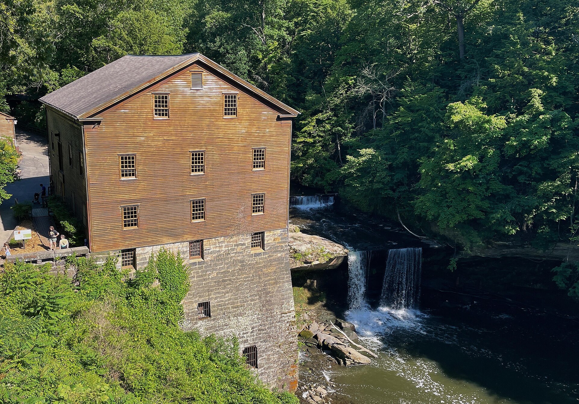 Lanterman's Mill and its waterfall among green woods in Youngstown's Mill Creek Park on a sunny day.