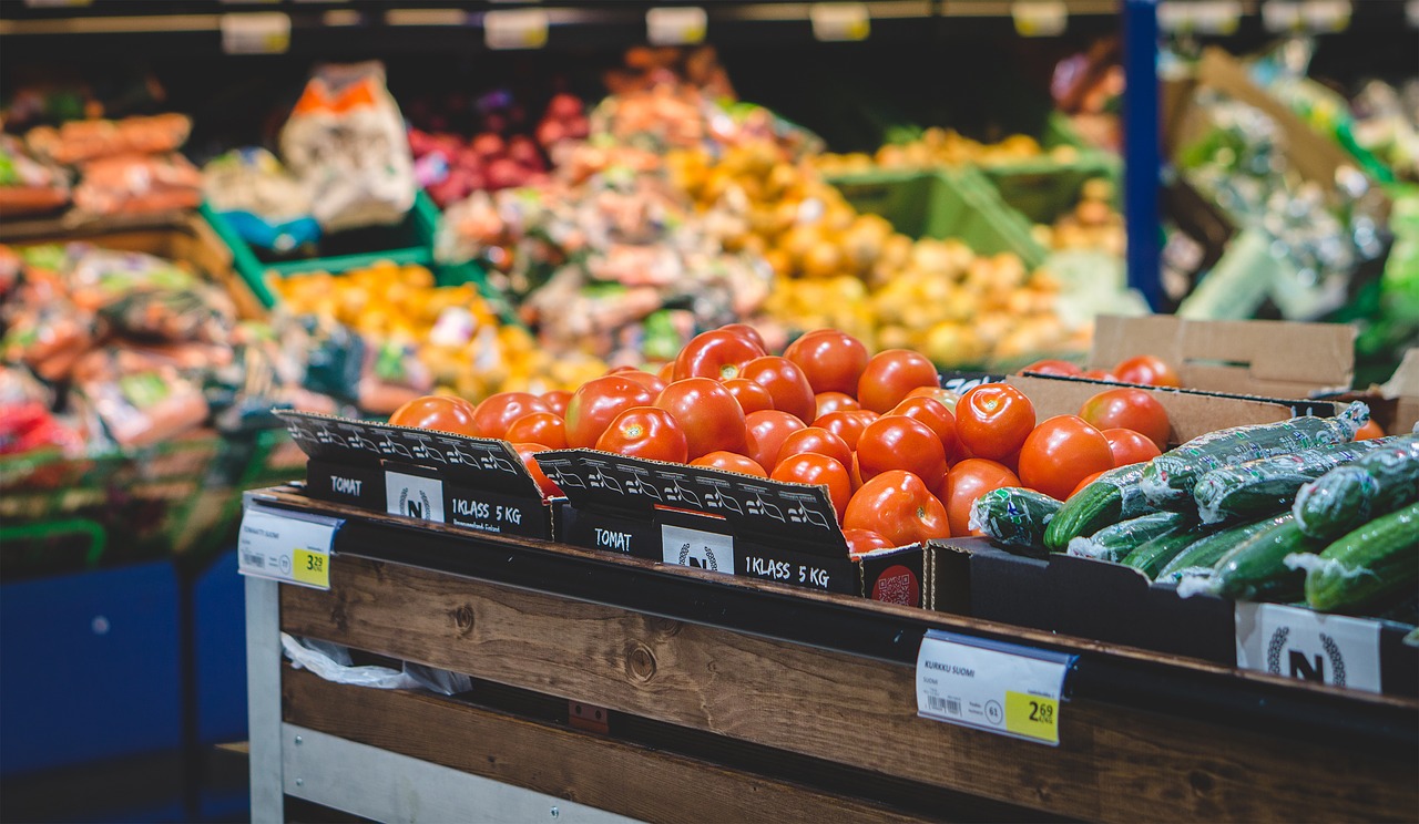 Tomatoes and cucumbers in crates on a supermarket produce stand, with more fruit and vegetables behind